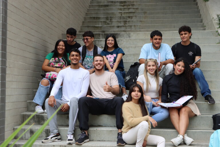 Group of diverse students sitting on concrete stairs outdoors, smiling and chatting together.